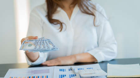 Young women holding dollar bills on the desk and graphsの写真素材