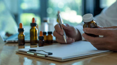 The doctor held a bottle of medicine and gave the medicine to the patient. The doctor sat at the desk in the office.の写真素材