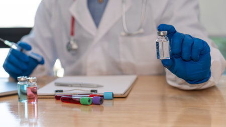 Doctors hold a vial of COVID-19 vaccine in a blue rubber glove in a close-up laboratory. Study the concept of coronavirus vaccination. On the table there was a bottle of experimental medicine and a noの写真素材