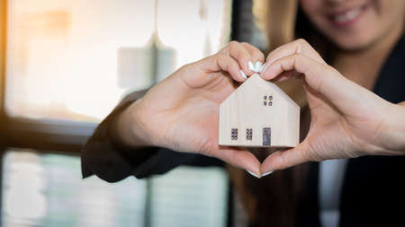 A young real estate officer or bank holding a small white house in the office. Home Loans, Dream...