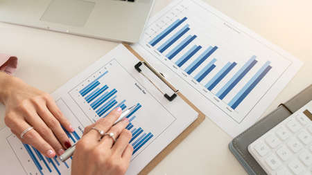 Young businesswoman analyzes cost graphs on desk in conference room with laptop