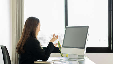 A beautiful Asian businesswoman is reviewing documents, graphs and discussions online via computer,...