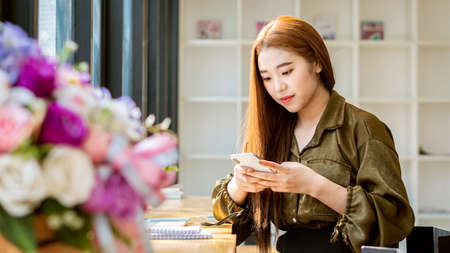 Asian female students studying computers and answering mobile phone messages in a coffee shop at...