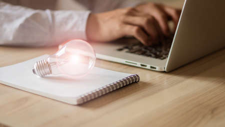 A business man in a gray shirt sitting in front of a laptop and a lamp next to him is thinking and thinking about the technology of work.の写真素材