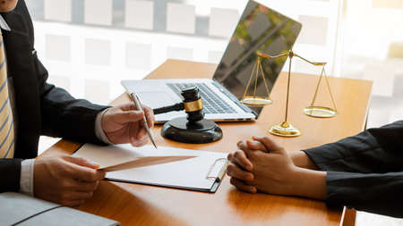 A lawyer advising clients at the desk in the office focuses on the hand with a hammer and scales on...