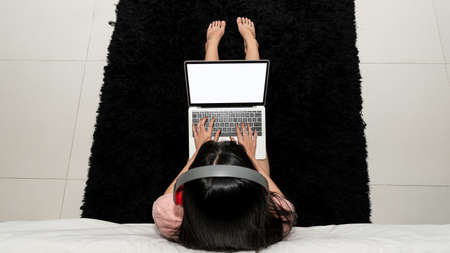A young woman working with a laptop sitting on the floor in the bedroom with a top view