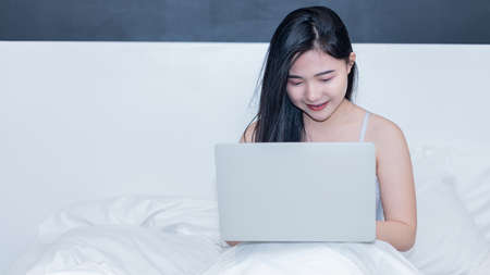 A young woman working with a laptop on a white mattress