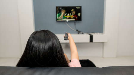 A young woman with a remote control watching tv alone in the bedroomの写真素材