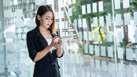 A charming Asian business woman sits at a desk and works with documents, graphs and laptops in the office.の写真素材