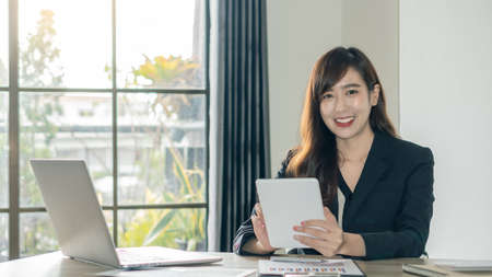 Young Asian businesswoman happily working on documents, graphs and laptops, smiling in the office.