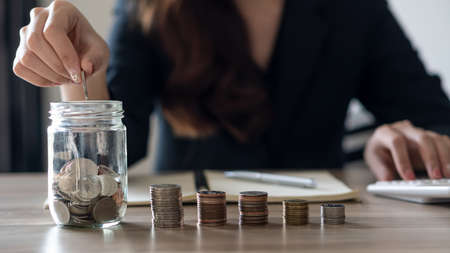 The hand of a young woman holding a coin in a pink jar to save money in the future.