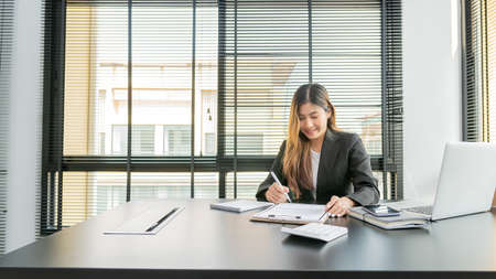 The lovely young Asian accountant enjoys working on computers and calculators in the office.の写真素材