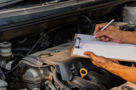 The auto mechanic checks the car engine with the check written in the car service engine repair...
