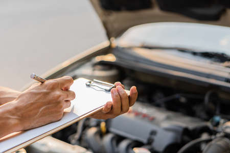 The auto mechanic checks the car engine with the check written in the car service engine repair...