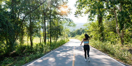 Slender beautiful girl in sportswear jogging along the road on a bright morning, girl running in the autumn forest. Back view. On the road. Outdoor shooting.の写真素材