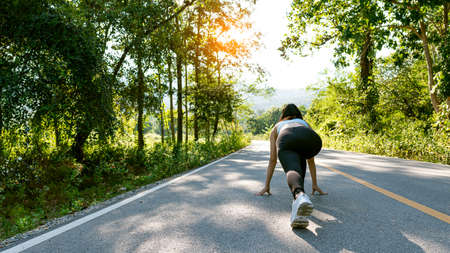 Slender beautiful girl in sportswear jogging along the road on a bright morning, girl running in the autumn forest. Back view. On the road. Outdoor shooting.の写真素材
