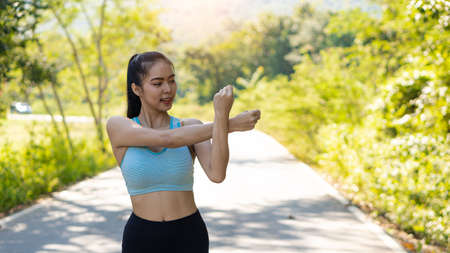 Asian women stretch before exercising for good health. Horizontal image while stretching in an outdoor park. A female runner warms up for an evening run and jogging.の写真素材