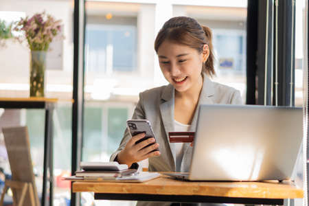Young Asian businesswoman using credit card and for financial payments and online shopping on laptops, retail stores, e-commerce, smartphones, smart payment transactions, money transfer technology.の写真素材