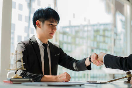 A male lawyer or judge consults a team with a female business client hand in hand. with hammer and scales concept of legal servicesの写真素材