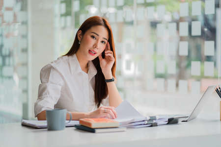 Young Asian businesswoman using a smartphone and Laptop, calculator on the desk. Independent woman...