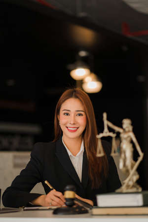 Attractive Asian Lawyer Female Lawyer Discussing Contract Documents with Golden Goddess Scales with Hammer on Wooden Tables in Office of Legal Services, Advice, Justice and Real Estate Ideas.の写真素材