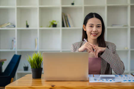 Asian businesswoman analyzing a report pointing to a graph with a pen, laptop, and calculator In her workstation, accountant, telemarketing ideas, e-commerce, free online marketing.の写真素材