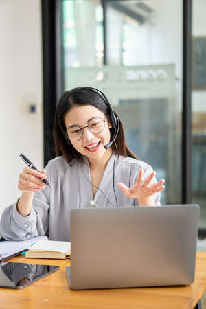 Asian college student wears wireless headphones and writes on a laptop to learn languages online...