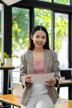 Happy Asian businesswoman standing in a suit holding financial documents in the office accounting conceptの写真素材