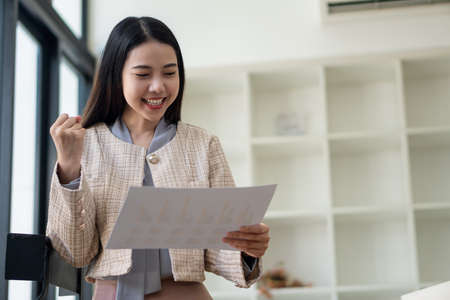 Happy Asian businesswoman standing in a suit holding financial documents in the office accounting...