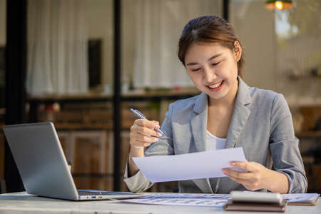 Young Asian businesswoman working on a laptop computer with a calculator in a bright modern office. Planning to analyze charts, business plans, investments, financial or accounting concepts.の写真素材