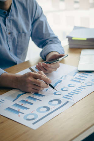 financial concept close-up businessman holding a graph pen press a calculator And make money by writing reports, memos and analyzing vertical image business documents.の写真素材