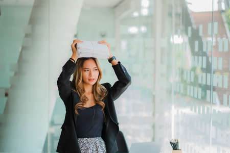 Asian businesswoman holding financial documents on her head and sideways in officeの写真素材