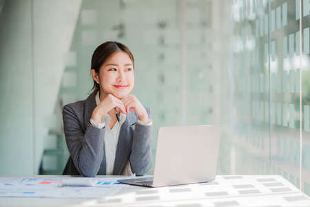 Attractive Asian businesswoman sitting on a computer in the office Prepare a report on the...