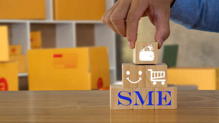 Businessman's hand holding wooden block, wooden cube laid on pile with hammer steam with yellow box business concept background smeの写真素材