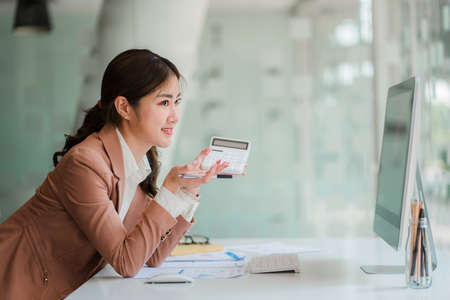 Asian businesswoman analyzing a report pointing to a graph with a pen, laptop and calculator. In the...