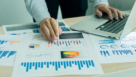 Close-up photo. Businessman holding pen and pointing at financial documents with financial marketing network diagram and working on laptop computer. online accounting conceptの写真素材