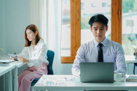 The concept of working together for young handsome and beautiful youngsters working on financial accounting and graphing, analyzing, and calculating documents with the laptop on aの写真素材