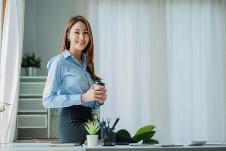 Businesswoman working in the office during coffee break smiling at the window giving a clear vision of work and success instilling trust in finance business idea.の写真素材