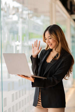 Asian businesswoman using laptop happily in office video greeting friends online telecommunication...