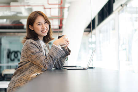 Young Asian businesswoman working with laptop computer on office desk and freely typing notebook. Lifestyle of women studying online business and education ideasの写真素材