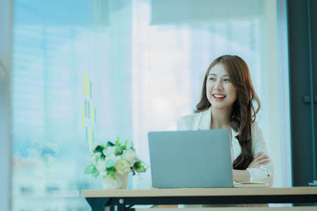 Young Asian businesswoman working with laptop computer on office desk and freely typing notebook. Lifestyle of women studying online business and education ideasの写真素材
