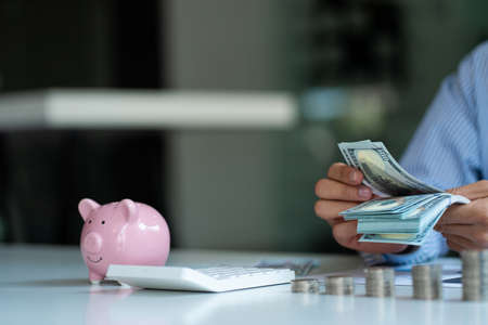 Businessman counting money with piles of coins and piggy bank calculator next to the money-saving concept.の写真素材
