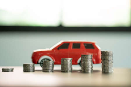 The red car is behind the pile of coins. all on the wooden table money saving ideas close-up images Save money for new car purchases, savings and car loans.の写真素材