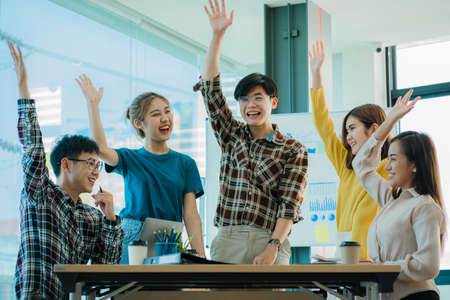 A group of creative young Asians in casual wear join hands to celebrate the success of their office project. Many men and women stood together at the beginning. teamwork concept ofの写真素材