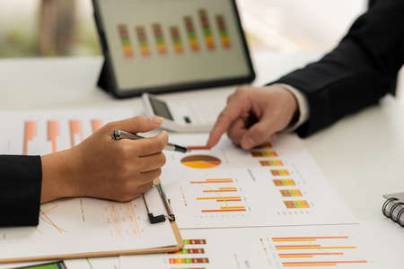 Two business partner colleagues discuss financial and company planning graphs during budget...