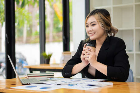 Young Asian businesswoman working on a laptop computer with a calculator in a bright modern office. Planning to analyze charts, business plans, investments, financial or accountingの写真素材