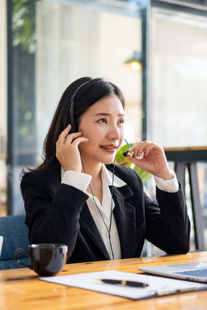 Charming and smiling Asian female customer service worker wearing headset in online meeting office look at laptop computer screen, work and social distancing concept, financial busの写真素材