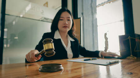 Attorney's Office. Hammer and scales of justice and attractive Asian female lawyer working in a law...