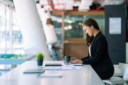Asian businesswoman working using laptop computer in modern office Make an account analysis report with financial graphs and real estate investment data. financial and tax system cの写真素材