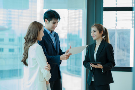 A young multi-ethnic business team in a high-key office sits on a laptop and does paperwork with happy smiles. Group of Asian businessmen team meeting in modern office Design and Cの写真素材